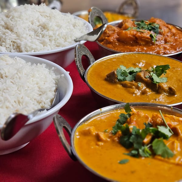 Bowls of white rice and three different curries with cilantro on a red tablecloth.