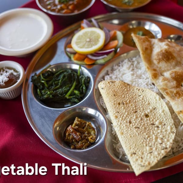 A Vegetable Thali with rice, naan, papadum, spinach, salad, and various curries on a red tablecloth.