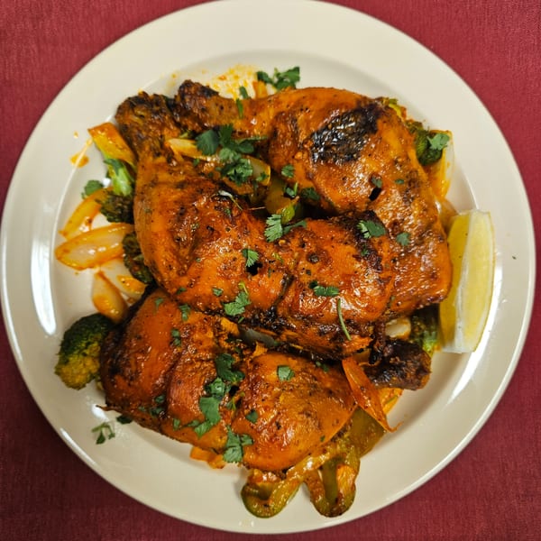 Four pieces of Tandoori Chicken with vegetables and a lemon wedge on a white plate.