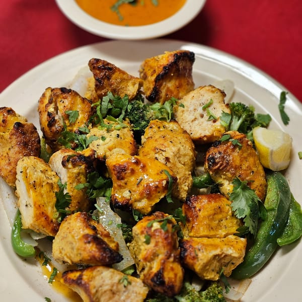 Grilled chicken tikka pieces with cilantro, broccoli, bell peppers, and a lemon wedge.