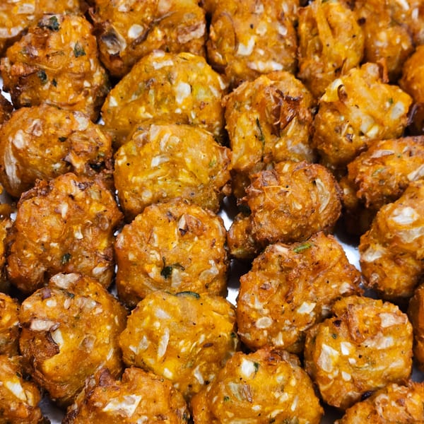 Close-up of numerous golden-brown, crispy fried fritters with visible vegetable pieces.