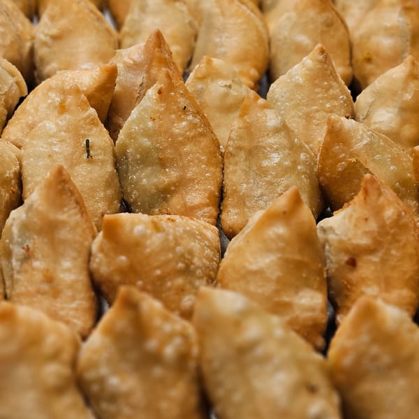 Close-up of many golden-brown, triangular samosas arranged in rows, showcasing their crispy texture.