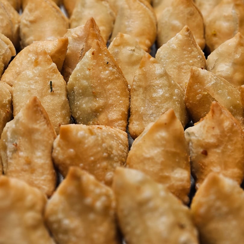 Close-up of many golden-brown, triangular samosas arranged in rows, showcasing their crispy texture.