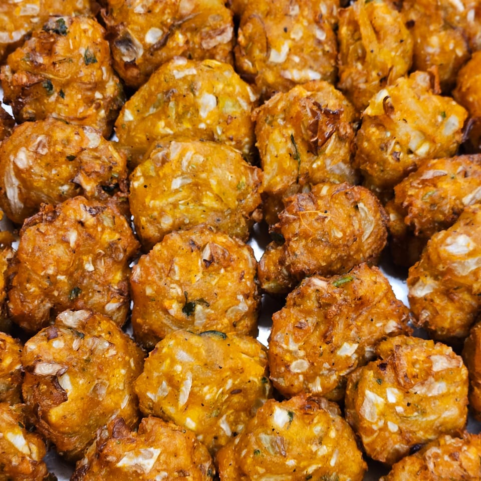 Close-up of numerous golden-brown, crispy fried fritters with visible vegetable pieces.