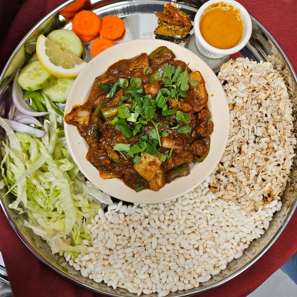 A Nepali thali with chicken chili, puffed rice, salad, carrots, and dipping sauces.